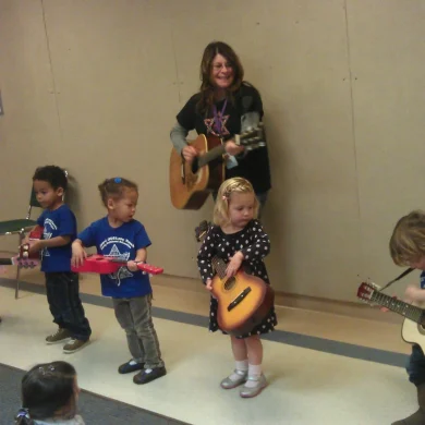 HaMo'Robyn Solovei playing guitar while teaching young children with toy guitars